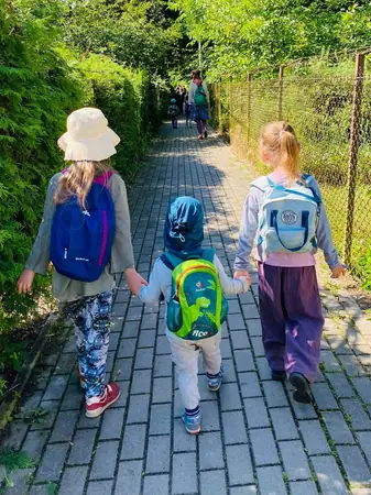 Troje dzieci z plecakami idzie chodnikiem, widziane od tyłu