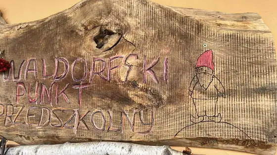Drewniana tablica z wypalonym napisem Waldorfski Punkt Przedszkolny i krasnalem