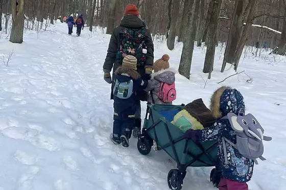 Grupa idzie leśną drogą zimą, dorosły ciągnie wózek transportowy
